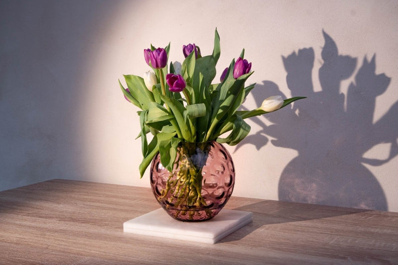 Violet Kugel Vase on a wooden table with white and purple flowers, as well as a white background and flower shadows 