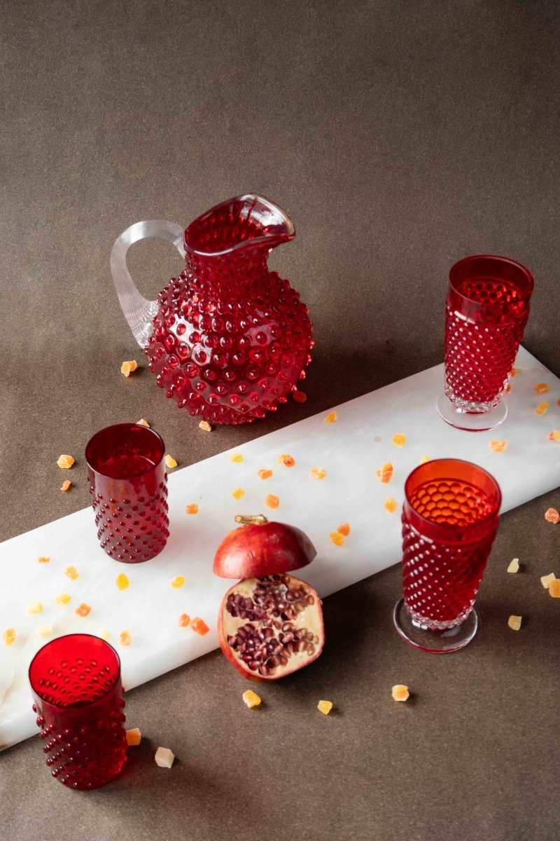 Underlay Garnet Hobnail Goblet (set of 2 pieces) surrounded by products from the Hobnail collection and fruit on a black background 