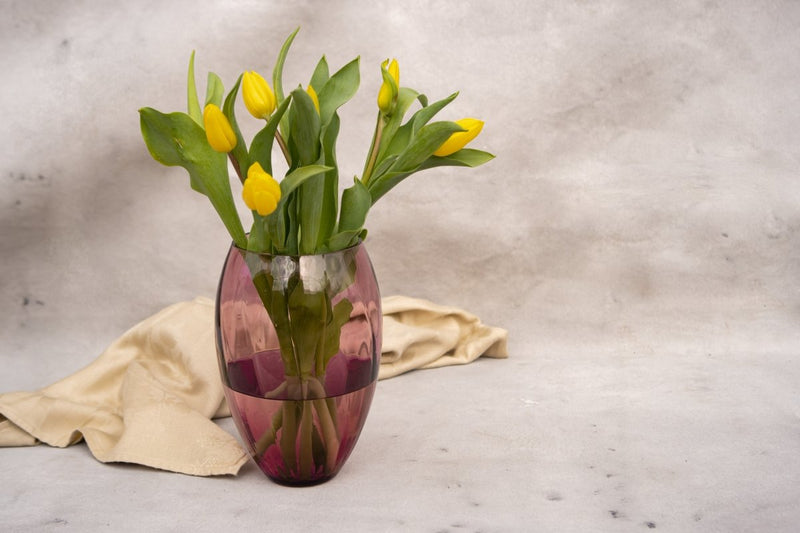 Violet Marika Vase Tall with yellow flowers, light yellow fabric and a white background